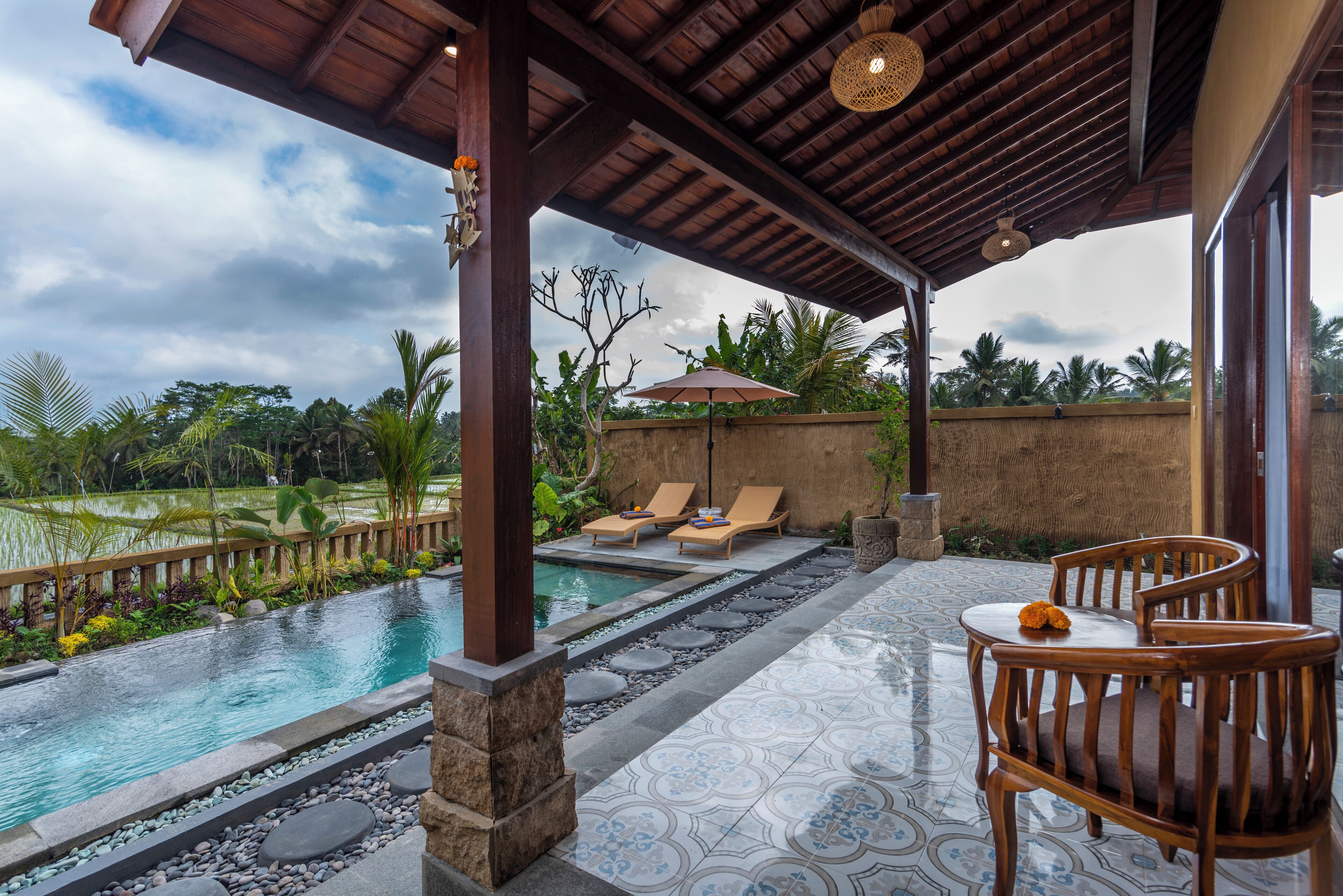 A covered outdoor area with a pool, lounge chairs, and a table.