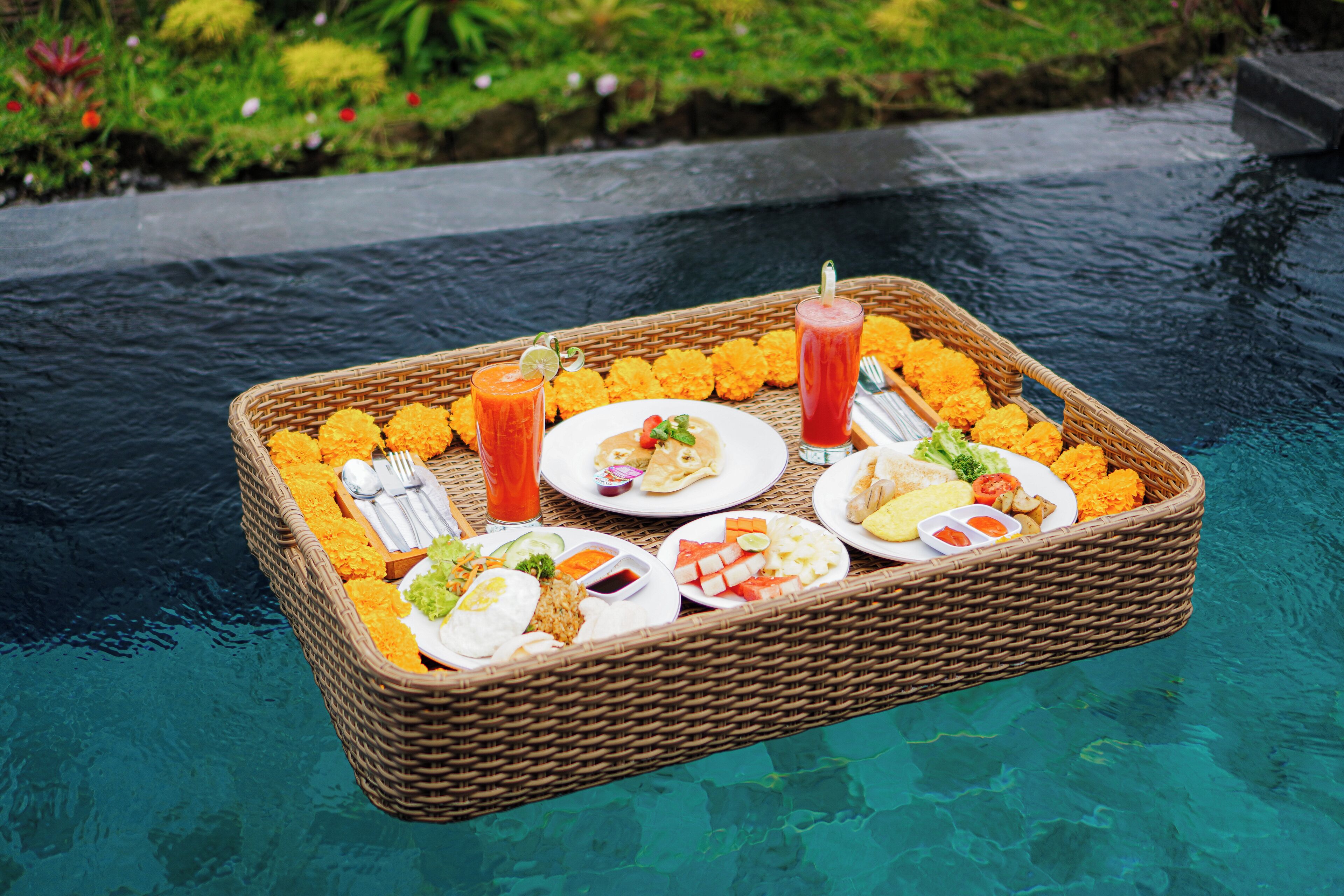A floating dining setup with a basket containing plates of food, drinks, and utensils, floating on a body of water.