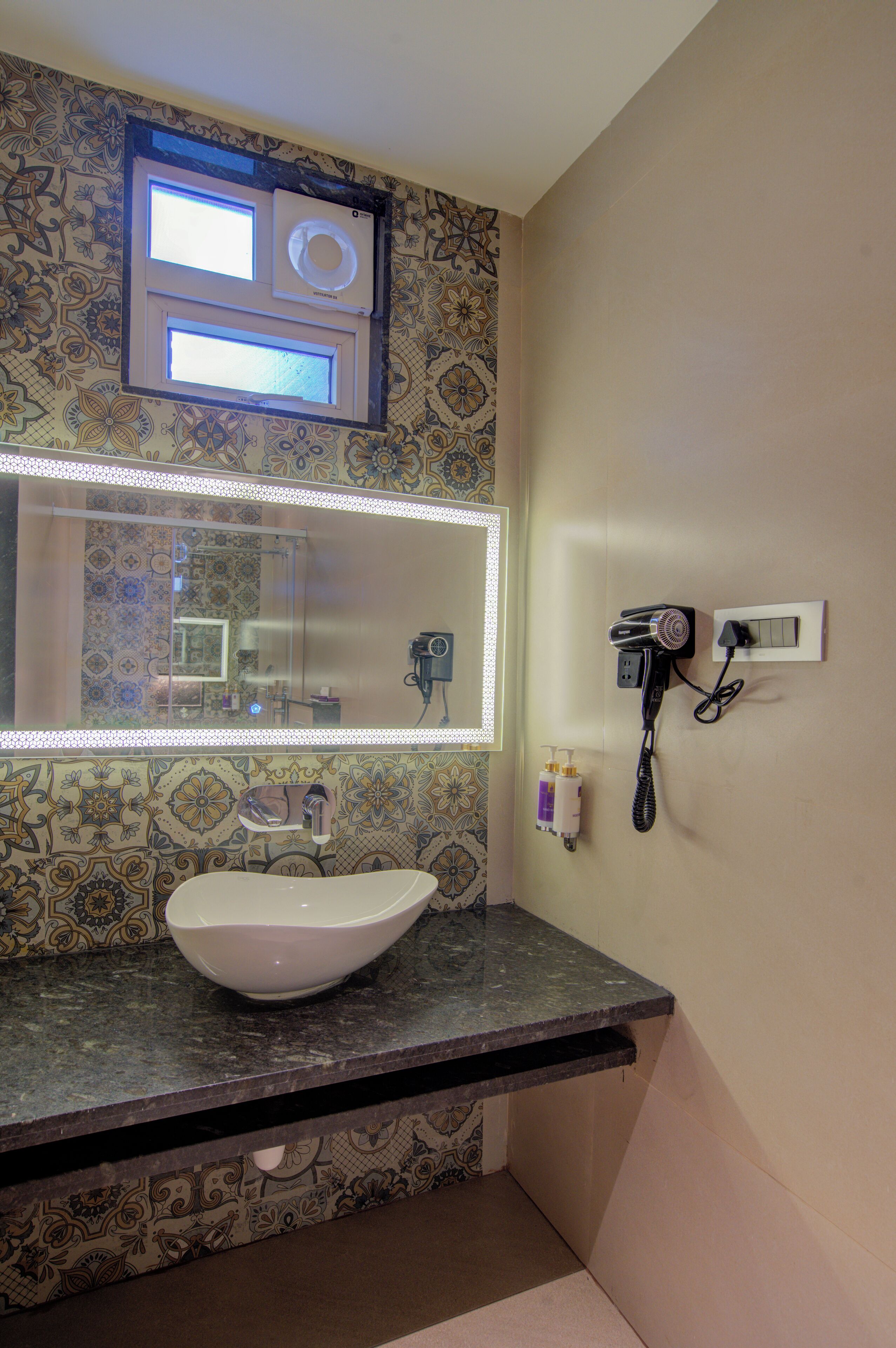 A bathroom with a large mirror, a sink, a hairdryer, and a wall-mounted hairdryer.