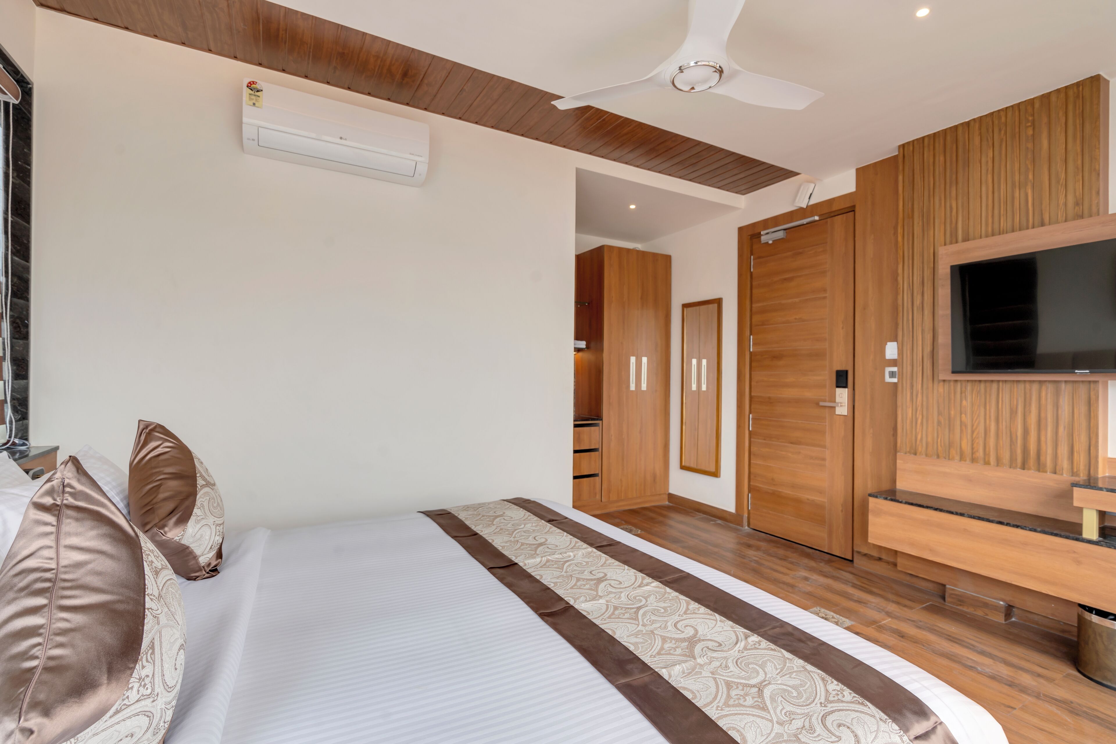 A modern bedroom with a large bed, wooden wardrobe, and a TV mounted on the wall.