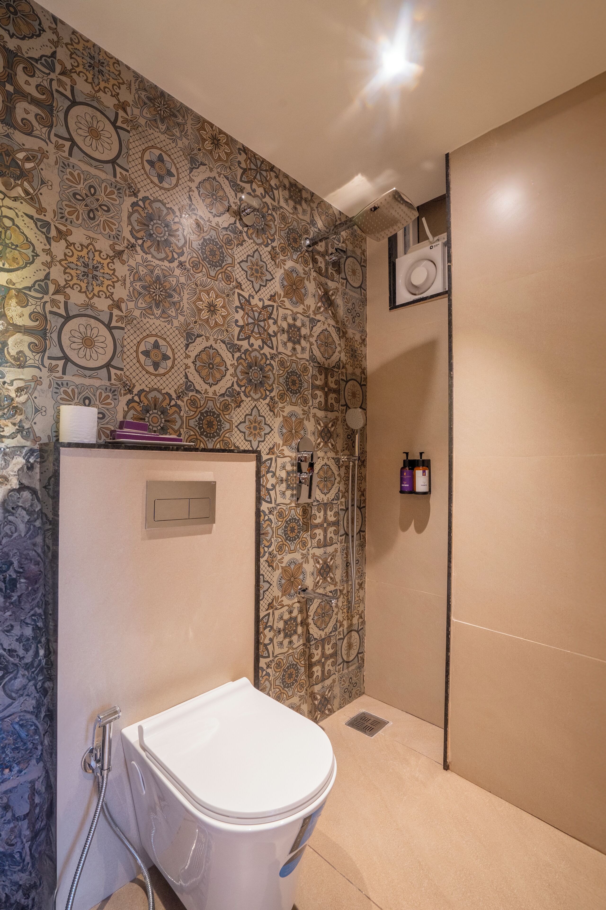 Un baño con pared de azulejos estampados, un inodoro, zona de ducha y un perchero con artículos de aseo.