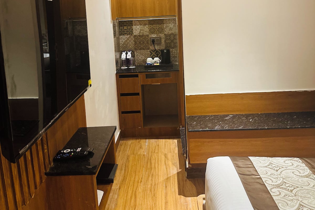 Une chambre d’hôtel compacte avec un plancher en bois, un téléviseur intégré, une petite kitchenette et un lit avec une literie à motifs.