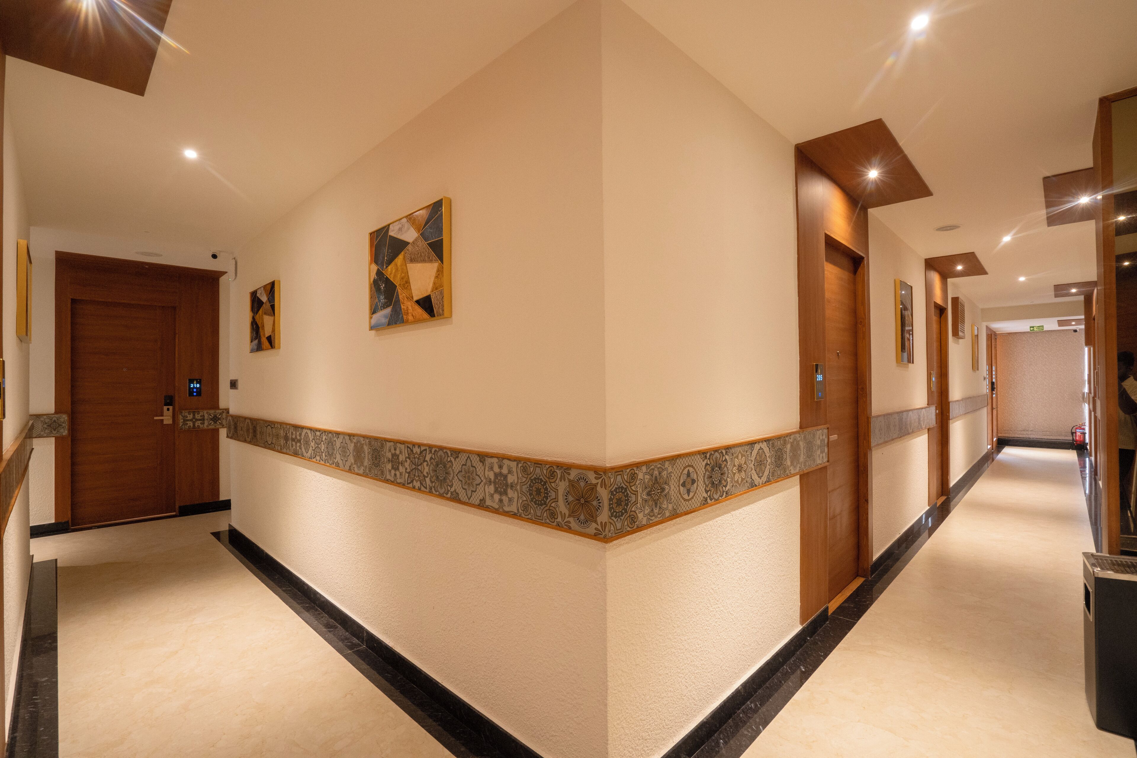 A hotel corridor with wooden doors, a patterned border, and artwork on the walls.