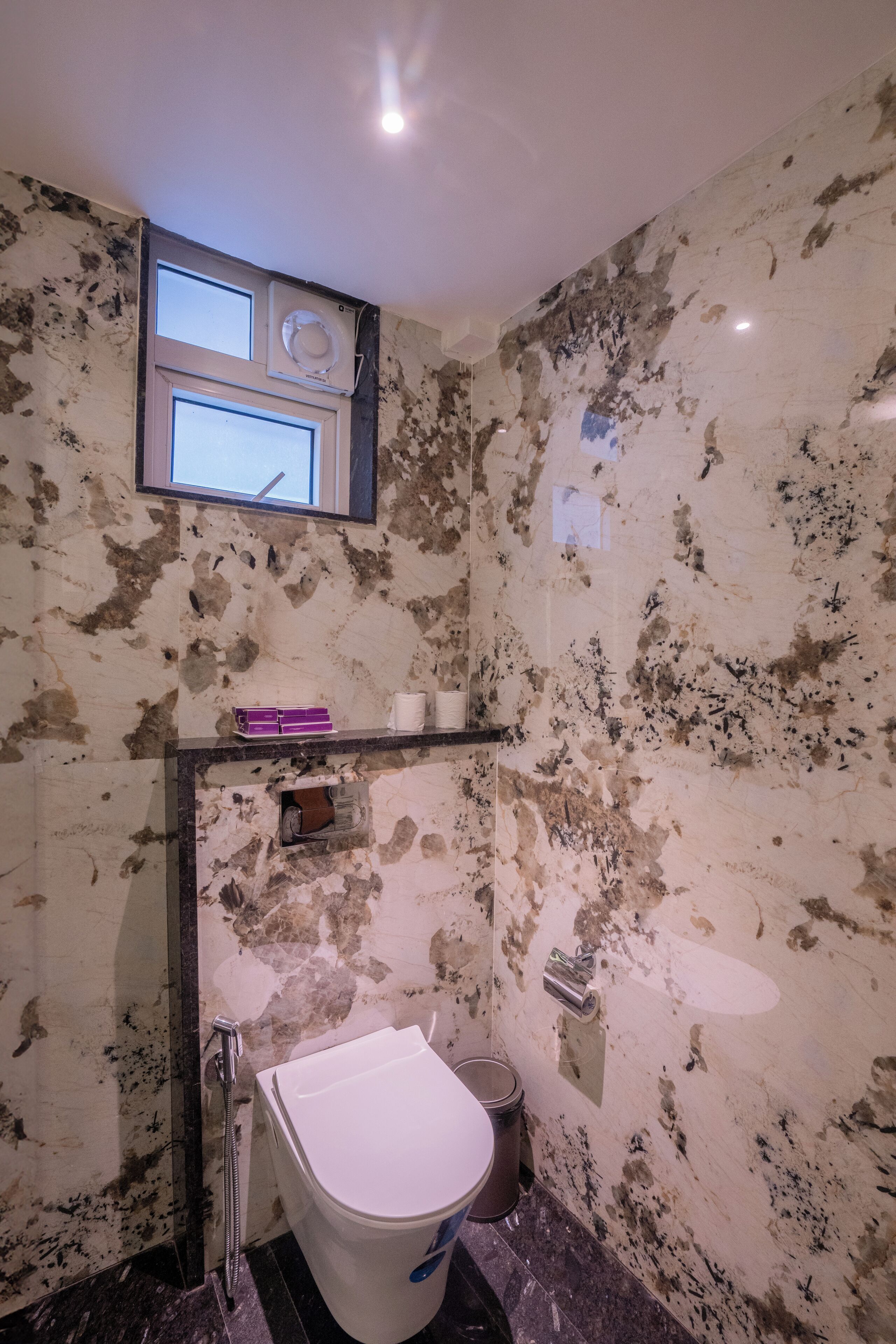 A bathroom with a white toilet, a shower, and a small window above the sink.