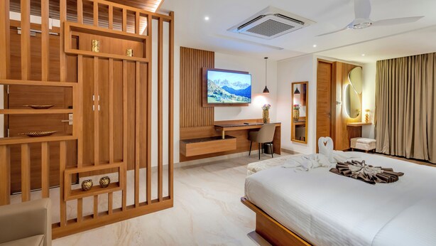 A modern hotel room with a wooden partition, a bed, a desk, a television, and a ceiling fan. - Park Avenue Hotel (Bengaluru)
