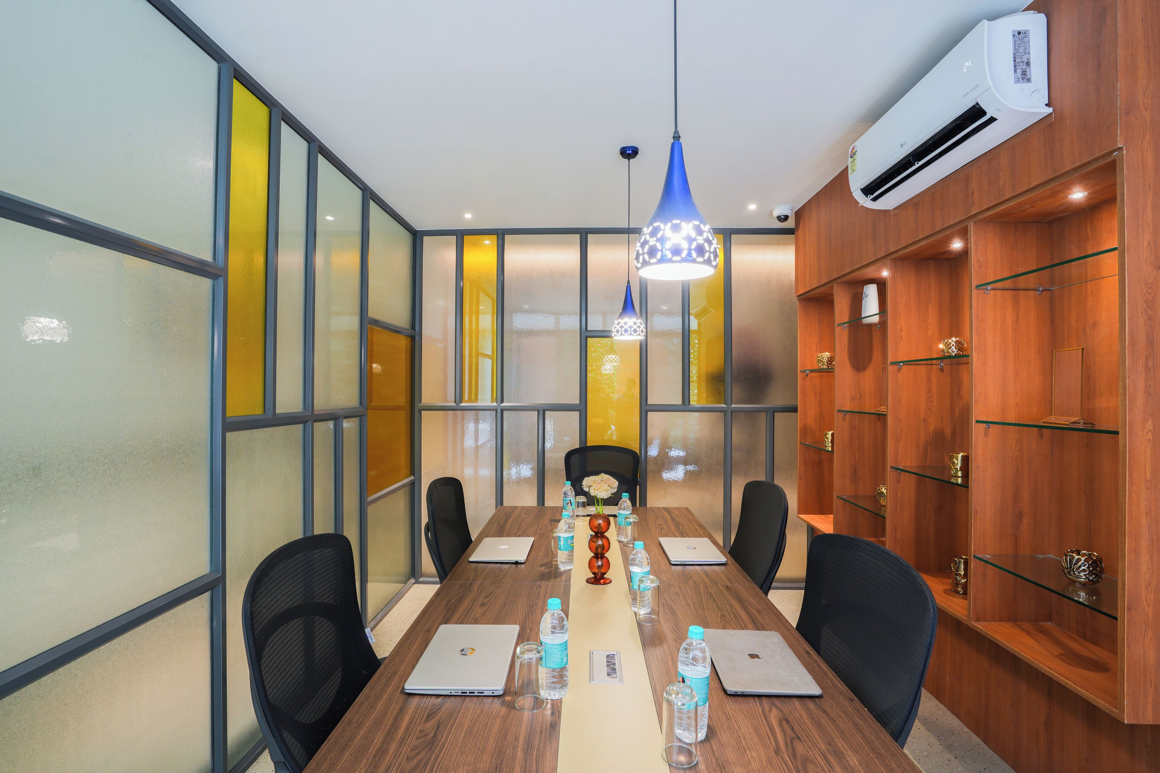 Un salón de conferencias con una larga mesa, sillas, computadoras portátiles, botellas de agua y elementos decorativos.