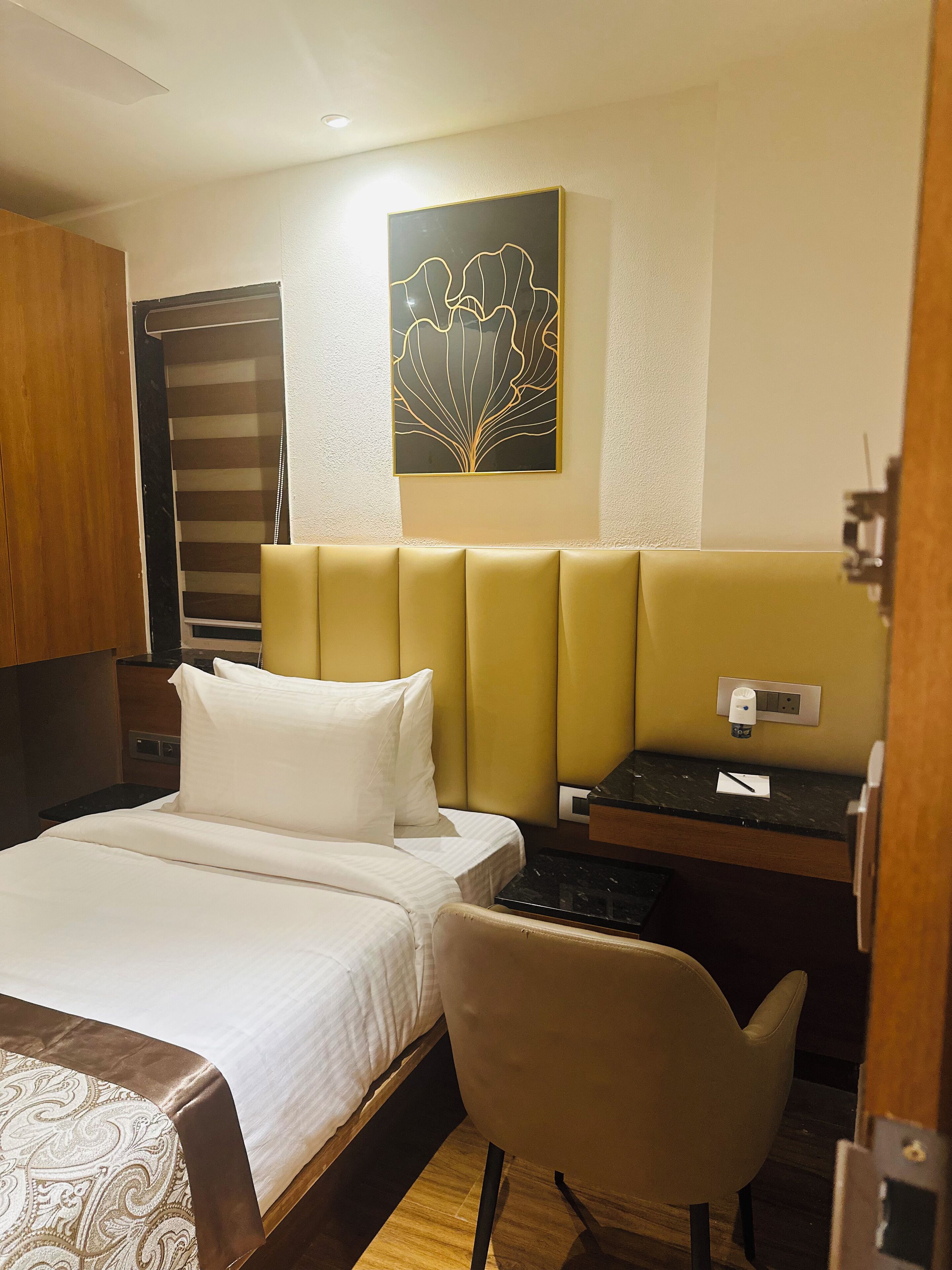 A hotel room with a bed, a desk, a chair, a wall art piece, and a door.