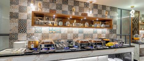 Zona de bufé con diversas estaciones de comida, recipientes etiquetados y un salpicadero de azulejos con diseño.