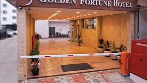 Indgangen til Golden Fortune Hotel med en træfacade, plantekasser og en sikkerhedsbarier.