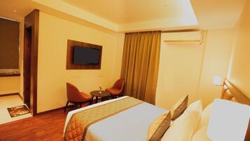 Habitación de hotel con cama, televisor montado en la pared, escritorio con silla y ventana con cortinas.