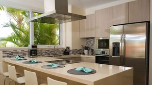 Een moderne keuken met een centraal eiland, roestvrijstalen apparatuur en uitzicht op palmbomen.