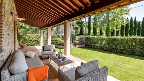 A covered outdoor seating area with wicker furniture and a view of a well-maintained garden. - Villa Vittoriano - Surrounded By Nature (Camaiore)