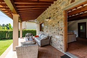 A covered outdoor seating area with wicker furniture, stone walls, and a wooden ceiling.