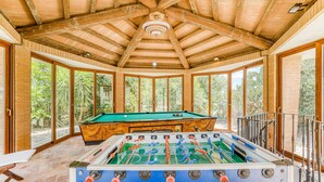 Un espacio interior amplio con mesa de futbolín, ventanas grandes y vigas de madera en el techo.