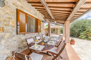 A stone-walled outdoor dining area with a wooden table set for six, surrounded by chairs.