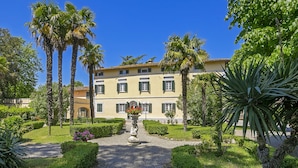 Un bâtiment à la façade symétrique, doté d’un jardin central avec une statue et bordé de palmiers.