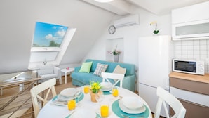 A modern, well-lit room with a dining table set for breakfast, a teal sofa, a small white table, and a kitchen area with a microwave. - Holiday home Škrika -Three Bedroom Home with heated Pool and Jacuzzi (Skrip)