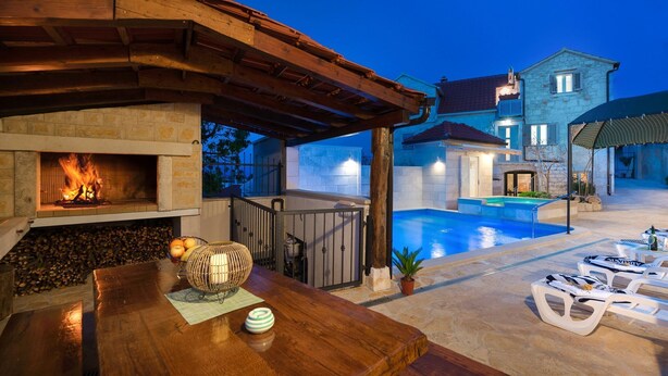 A patio area with a stone fireplace, a pool, and lounge chairs. - Holiday home Škrika -Three Bedroom Home with heated Pool and Jacuzzi (Skrip)