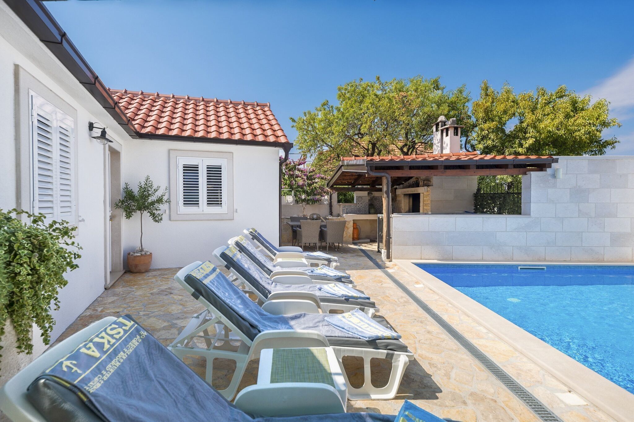 A poolside area with lounge chairs, a small outdoor kitchen, and a clear blue pool.
