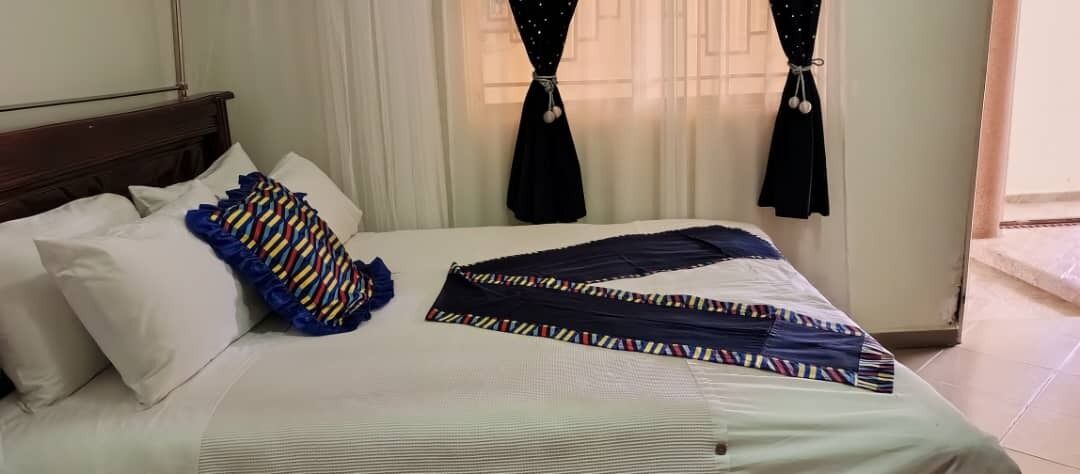 A neatly made bed with white linens, a striped blanket, and a colorful pillow.