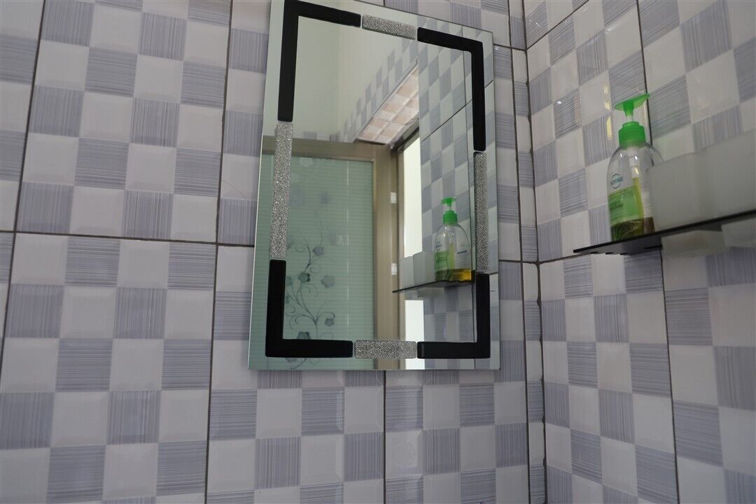 A bathroom with a checkered tile wall, a mirror with a black frame, and a shelf with toiletries.