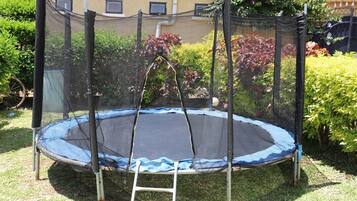 Enjoy bouncing fun in the backyard with a trampoline surrounded by lush greenery and a nearby building.