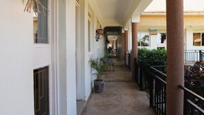 A covered corridor with potted plants, a tiled floor, and a railing on one side. - Hotel Judith (Gulu)