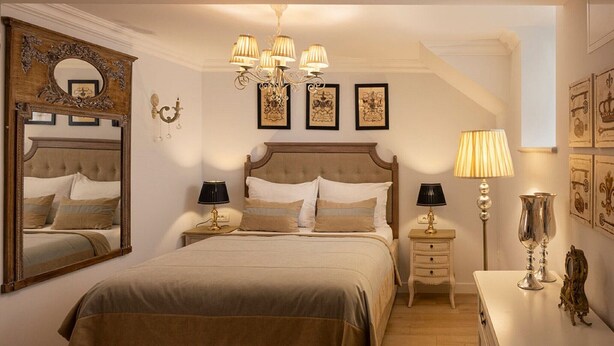 Un dormitorio con una cama grande, dos mesitas de noche, un candelabro y cuadros en las paredes.