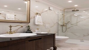 Un baño con tocador de mármol, espejo con marco dorado, ducha con cerramiento de vidrio y un inodoro.