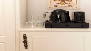 Una cafetera sobre un mueble blanco con un tirador decorativo, una jarra de vidrio y dos copas de vino.