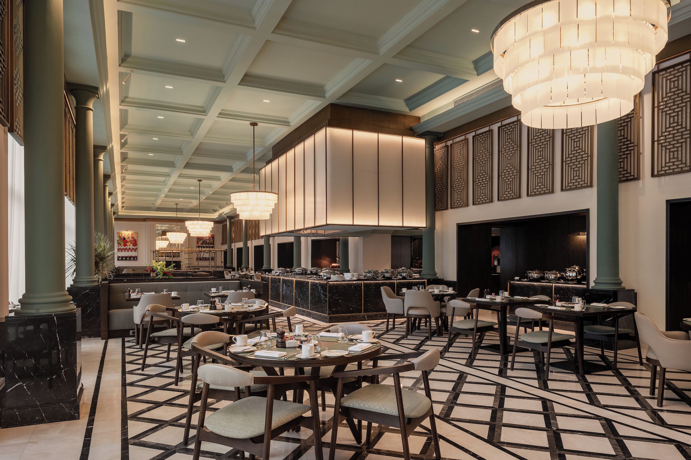 En rummelig hotellobby med et centralt barområde, flere siddepladser og et mønstret gulv.