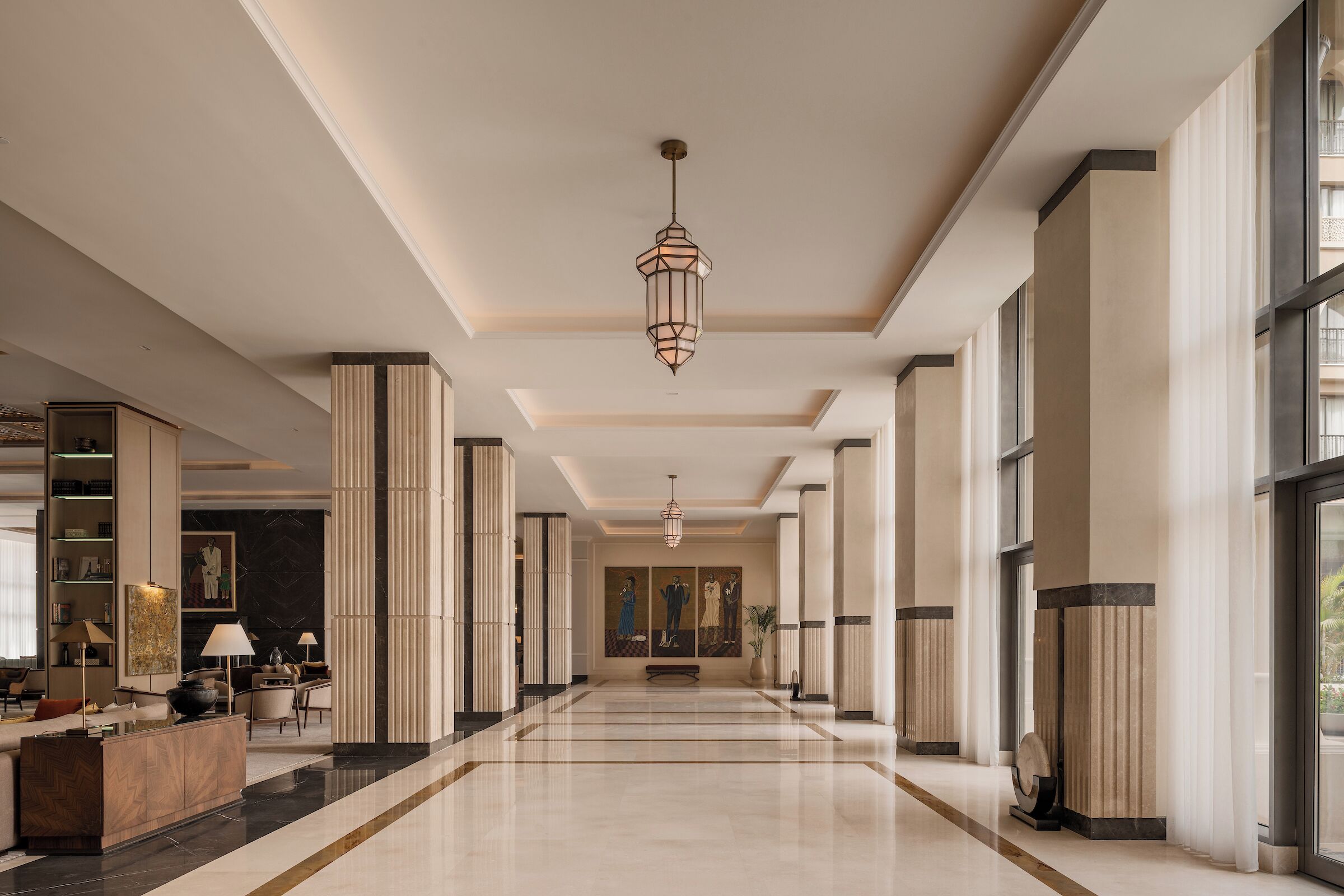 Un amplio vestíbulo de hotel con techo alto, una lámpara central y un largo pasillo que conduce a la entrada.
