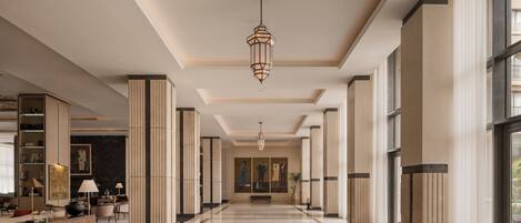 Un amplio vestíbulo de hotel con techo alto, una lámpara central y un largo pasillo que conduce a la entrada.