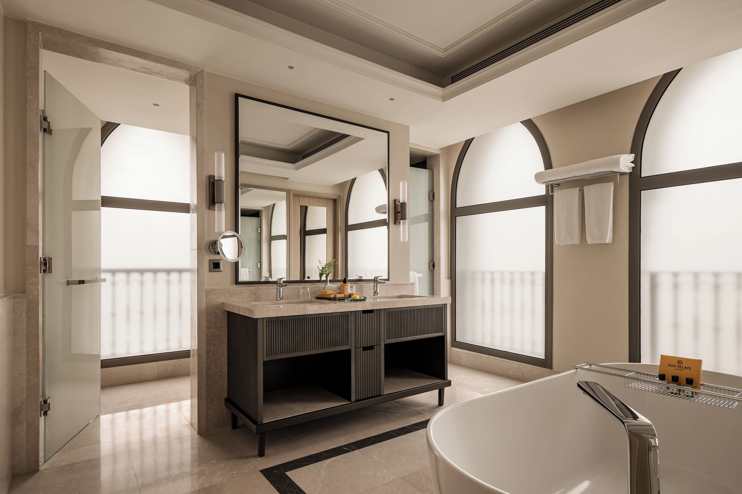 A modern bathroom with a large mirror, a freestanding bathtub, and a vanity with a sink and towel rack.