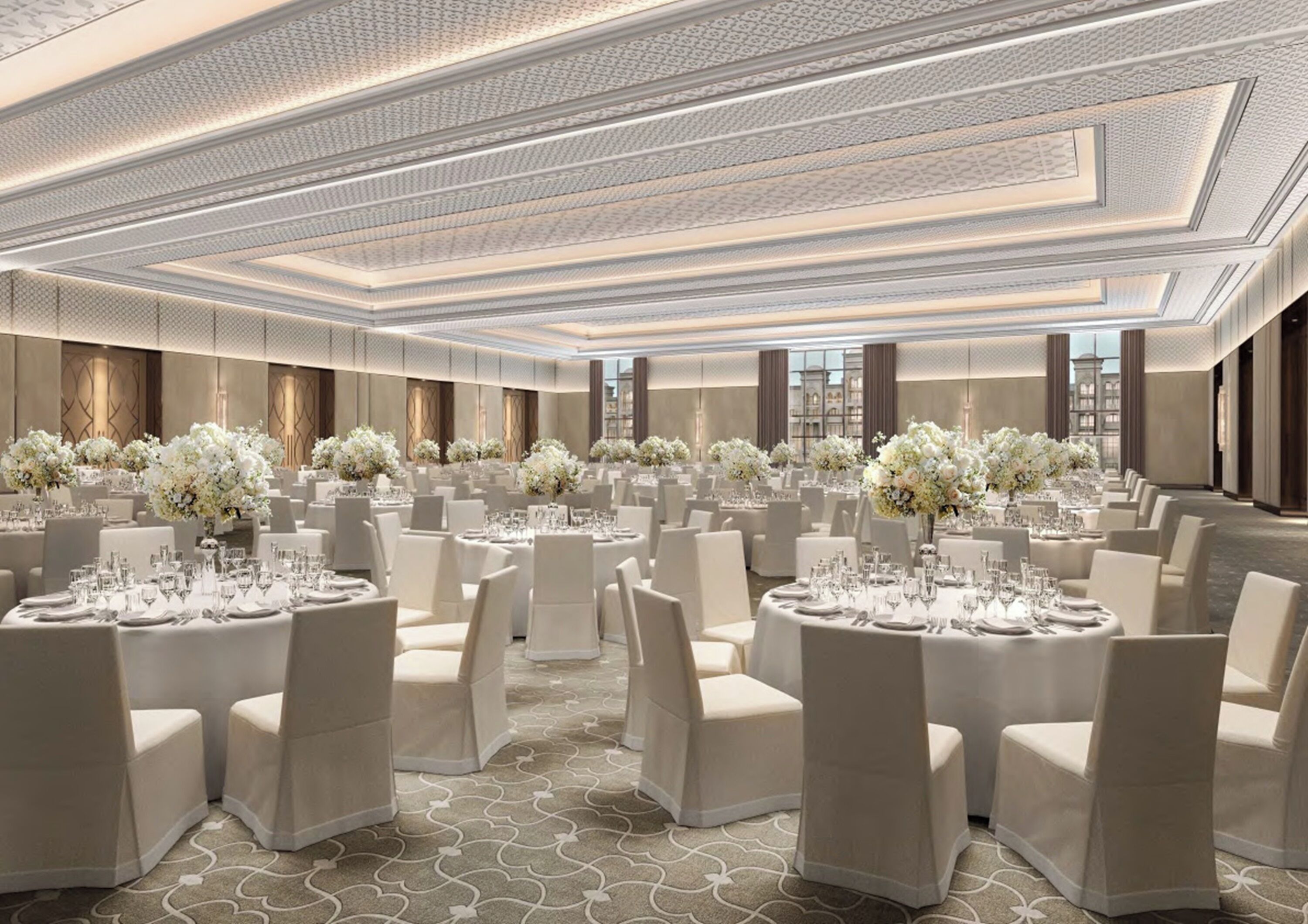Een ruime balzaal met ronde tafels, witte stoelen en bloemrijke decoraties.