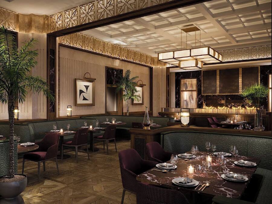 Ein Restaurant mit hoher Decke, Wandverkleidungen mit Muster und verschiedenen Sitzgelegenheiten, darunter Sitzeinheiten und Tische.