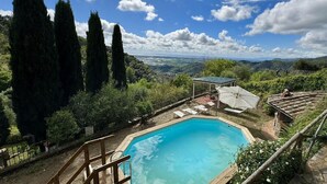 A pool with a wooden deck, surrounded by tall trees and a view of a valley. - Stone House in Chiatri with Lake Views (Lucca)