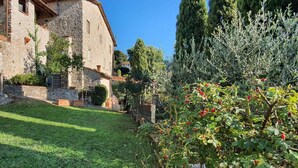 A stone building with a well-maintained garden and a large tree in the foreground. - Stone House in Chiatri with Lake Views (Lucca)