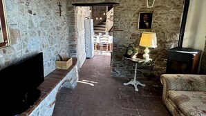 A rustic stone-walled room with a fireplace, a television, a table with a lamp, and a sofa. - Stone House in Chiatri with Lake Views (Lucca)