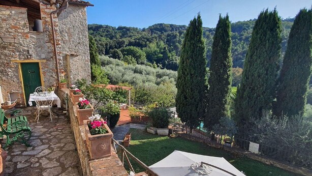 A stone building with a green door, outdoor seating, and a view of a lush hillside. - Stone House in Chiatri with Lake Views (Lucca)