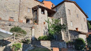 A stone building with a sloped roof, multiple windows, and a staircase leading to the entrance. - Stone House in Chiatri with Lake Views (Lucca)