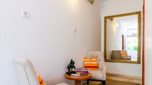 A room with two armchairs, a small table with books and a statue, and a mirror with a gold frame.