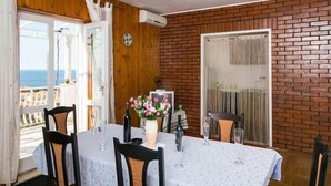 A dining area with a table set for two, a vase with flowers, and a view of the sea through a window.