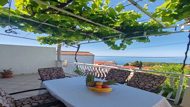 A terrace with a table set for dining, a white tablecloth, and a fruit bowl.