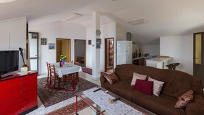 Un salón con un sofá marrón, un armario rojo, una mesa de comedor con sillas y una cocina al fondo.