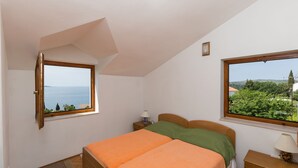 Un dormitorio con una cama, dos ventanas, una mesita de noche y una lámpara.