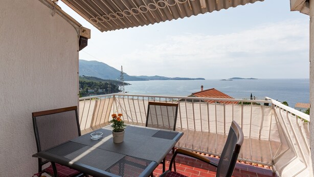 Un balcón con mesa y sillas, con vistas a la costa, montañas y el mar.