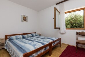 A bedroom with a wooden bed, a nightstand, a chair, a window with a view of trees, and a framed picture on the wall.
