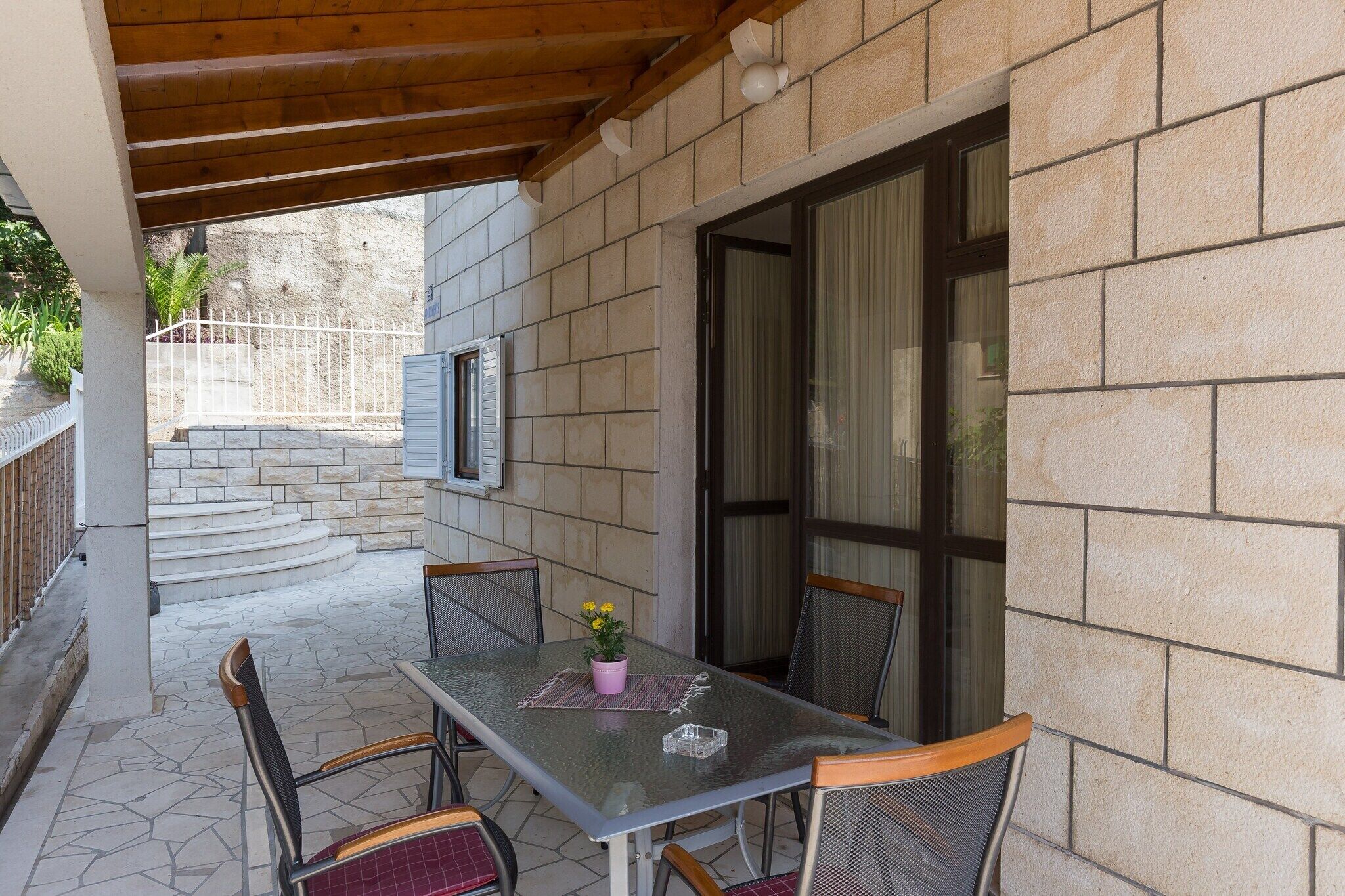Un patio al aire libre con una mesa, sillas, una planta en maceta y un muro de piedra.