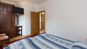 Une chambre à coucher comprenant un lit, une armoire, un téléviseur fixé au mur et une porte donnant sur une autre pièce.